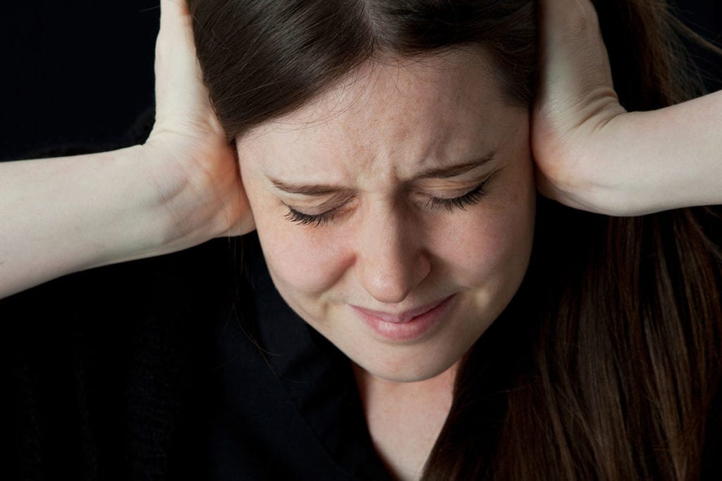 a woman covers her ears as someone tries to talk about disproven treatments for paranoid schizophrenia