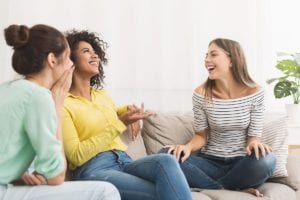 three women sit on a couch together laughing and talking about their aftercare programs