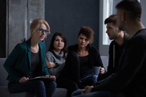 group of young people talk with older female therapist in a heroin addiction treatment center