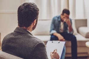 therapist takes notes while talking to struggling male patient in an opioid addiction treatment center