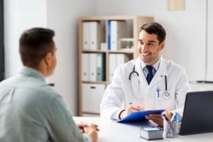 male doctor fills out form on clipboard for male patient after discussing partial hospitalization programs