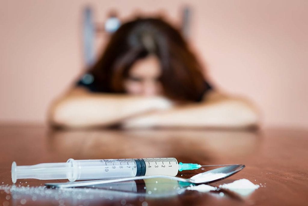 woman staring at syringe facing the signs of drug withdrawal laying her head down on the table