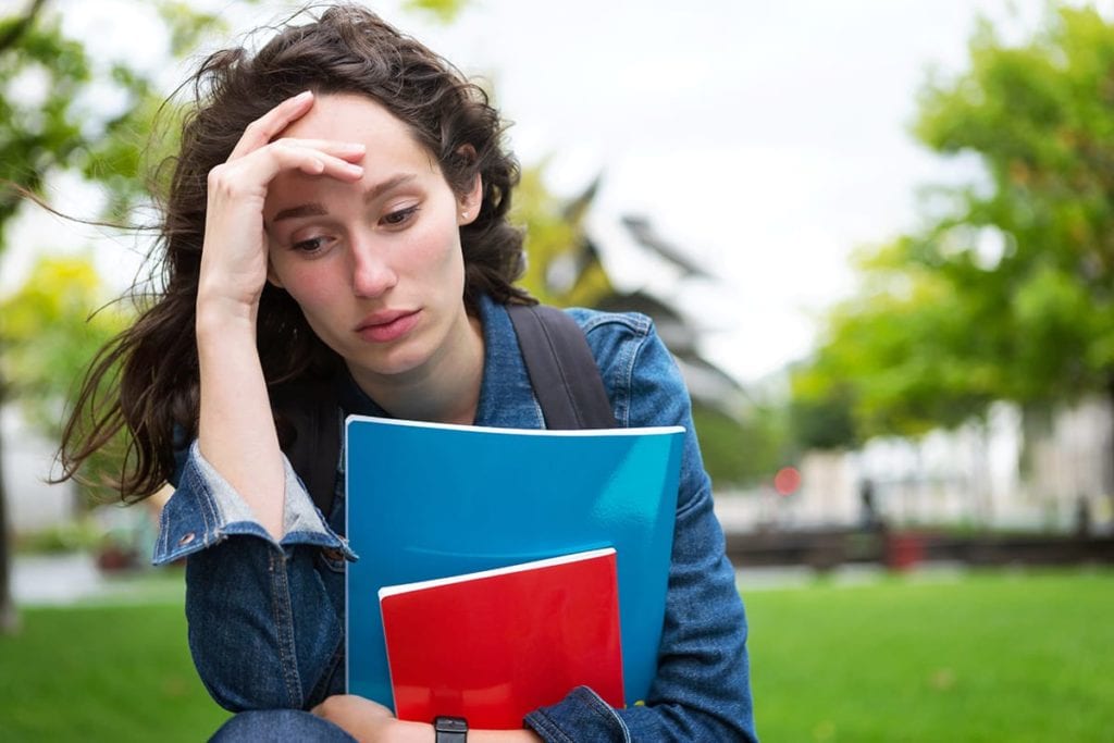 a woman puts her hand to her head after reading anxiety statistics on college campuses
