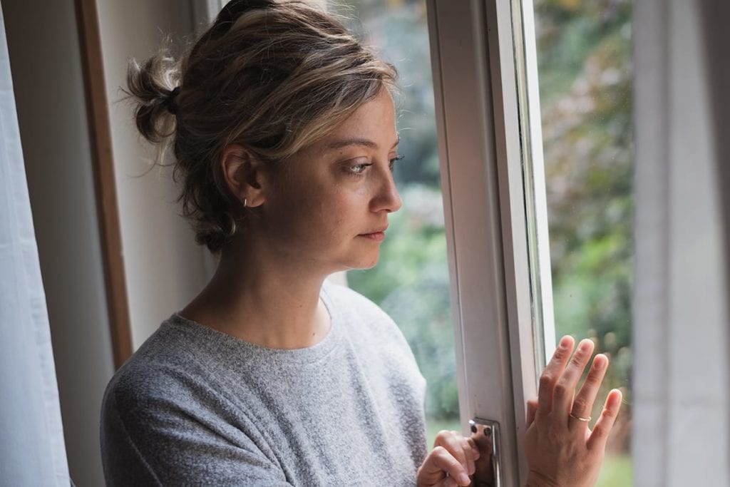 A woman stares out the window as she thinks about mental health acronyms