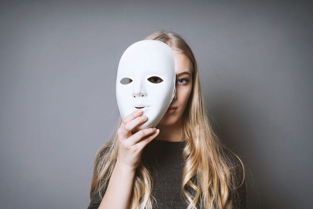 a woman holds a white mask in front of her face as she thinks about understanding borderline personality disorder relationships