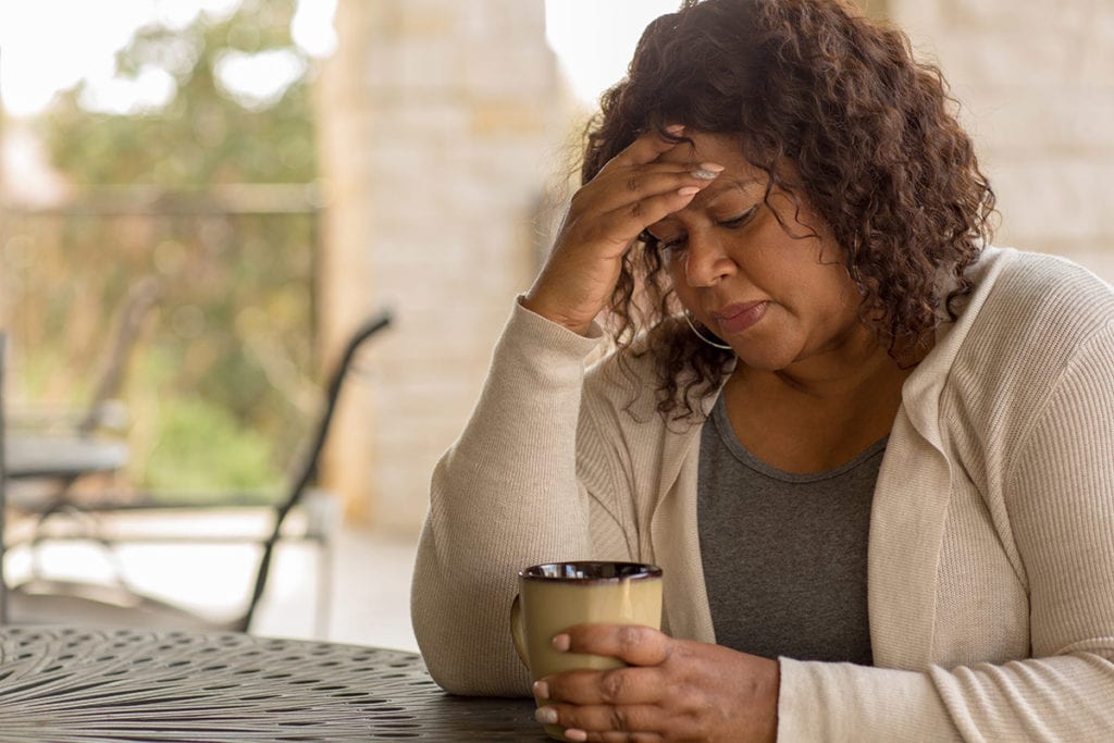 a woman holds her head and drinks coffee as she wonders how hard is it to quit drinking